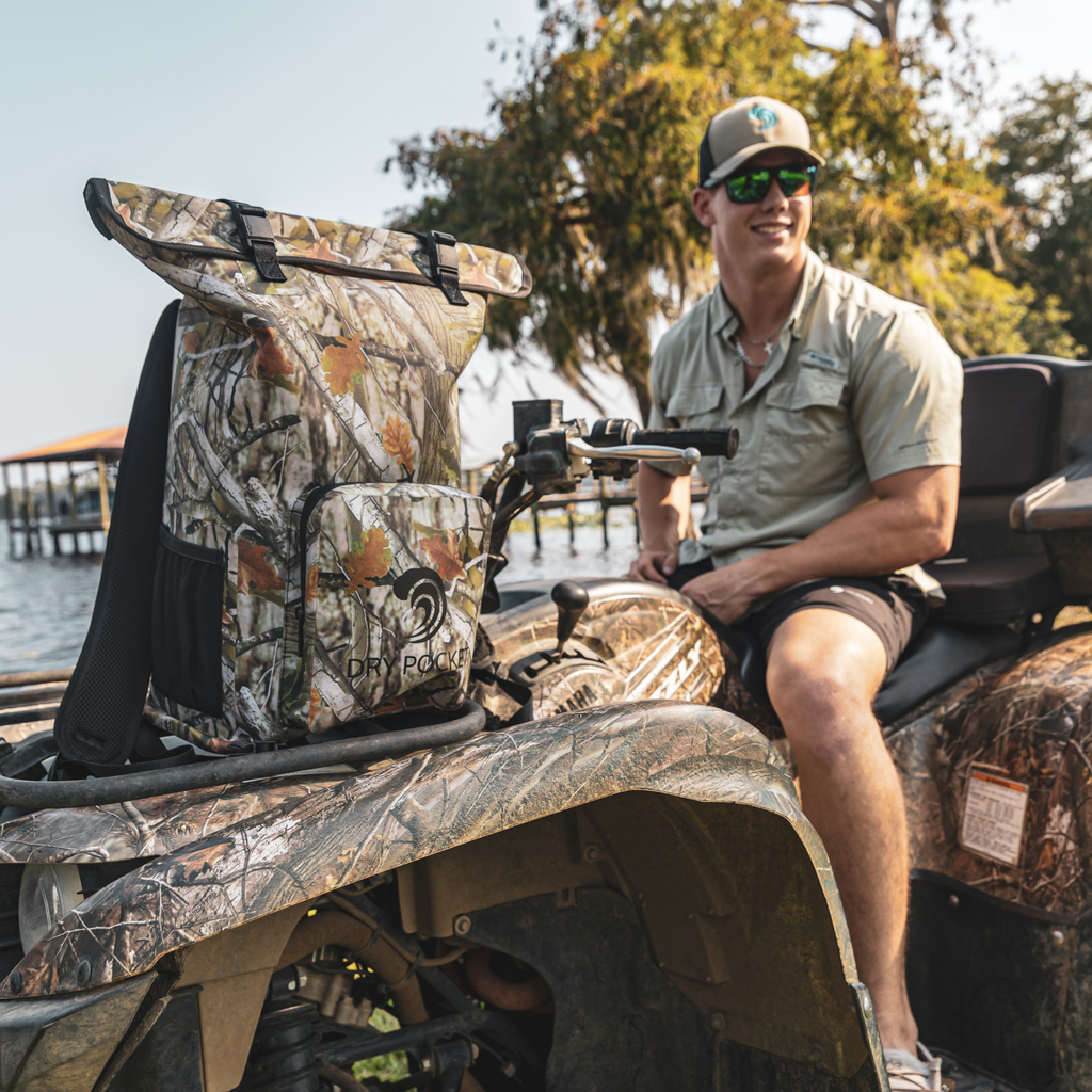 Forest Camo Dry Pocket backpack on the front rack of an ATV beside its rider.