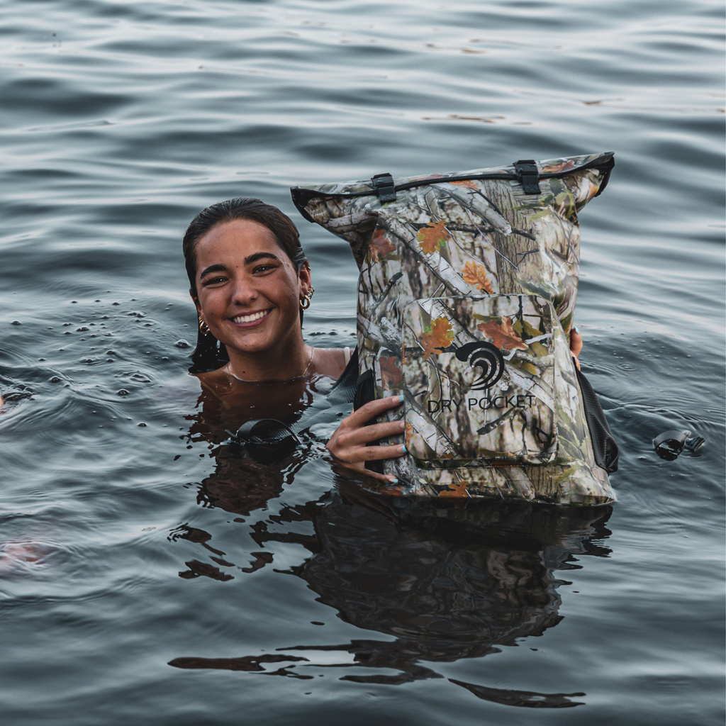 Person in the water holding a Forest Camo Dry Pocket backpack above the surface.