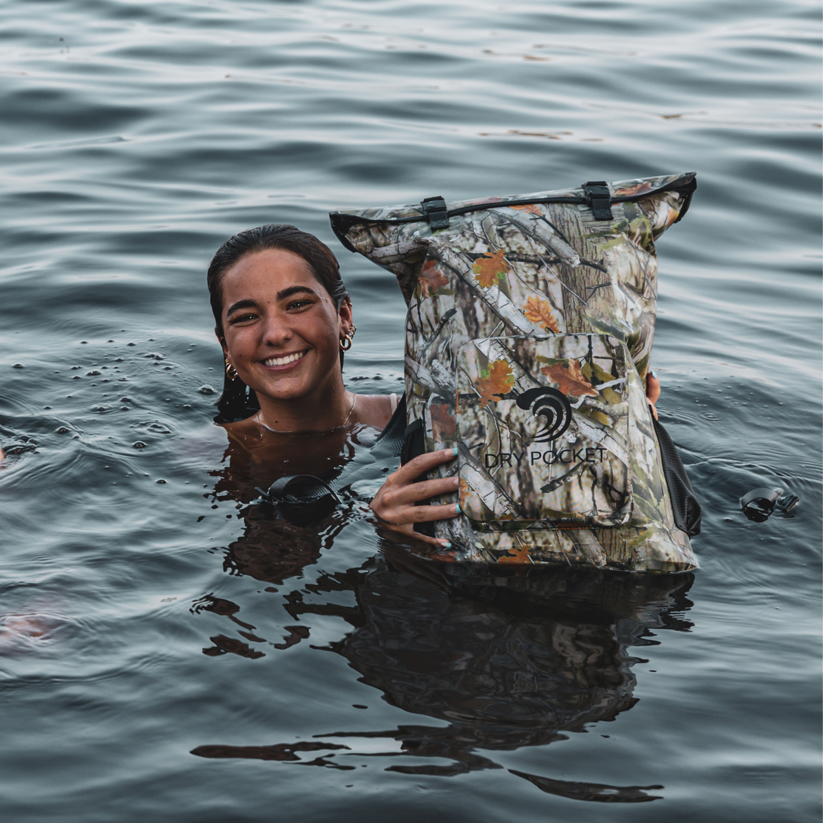 Person in the water holding a Forest Camo Dry Pocket backpack above the surface.
