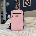 Pink COR Surf backpack standing upright on a bed.