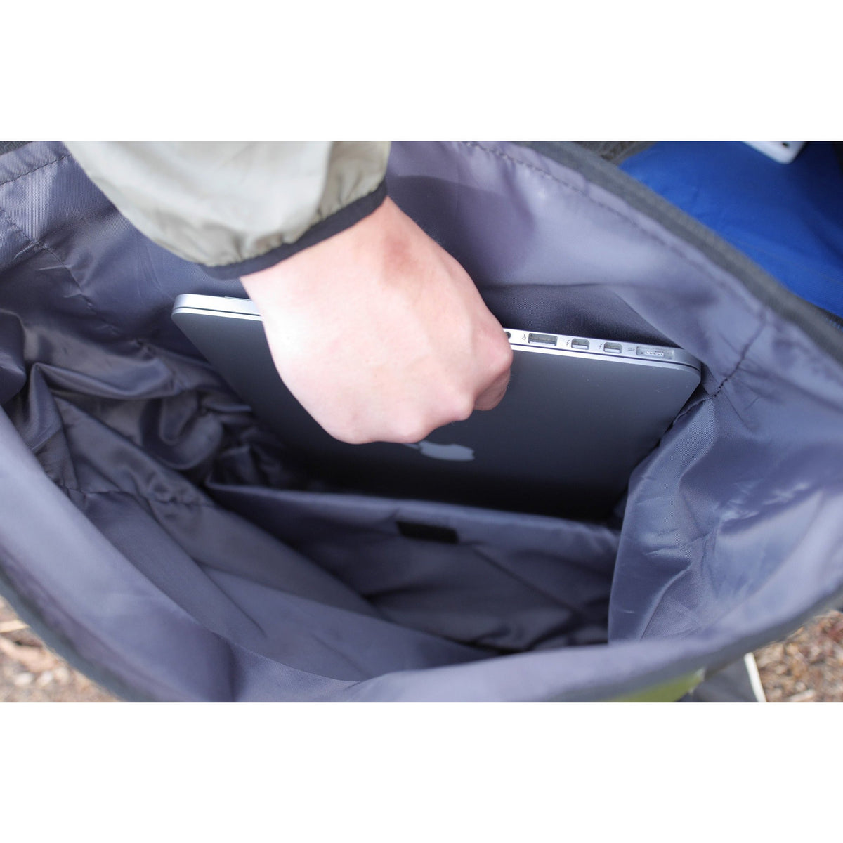 A hand placing a laptop into the padded sleeve inside the dry bag.