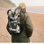 Person wearing a camouflage COR Surf dry bag backpack on a beach.